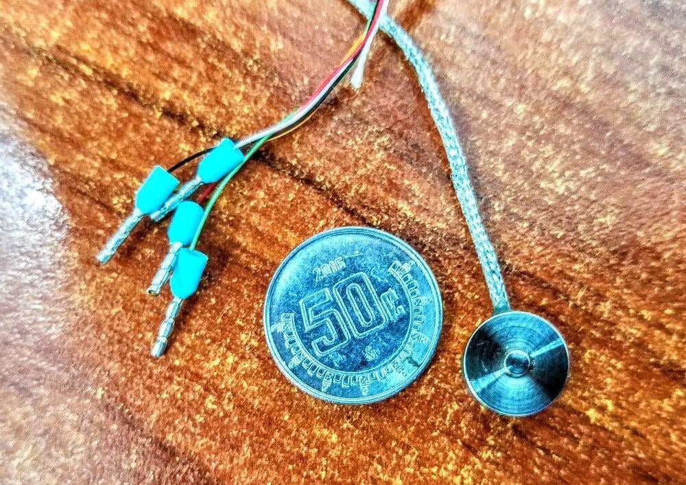 Sensor de carga tipo botón miniatura, se puede apreciar el tamaño comparado a una moneda.